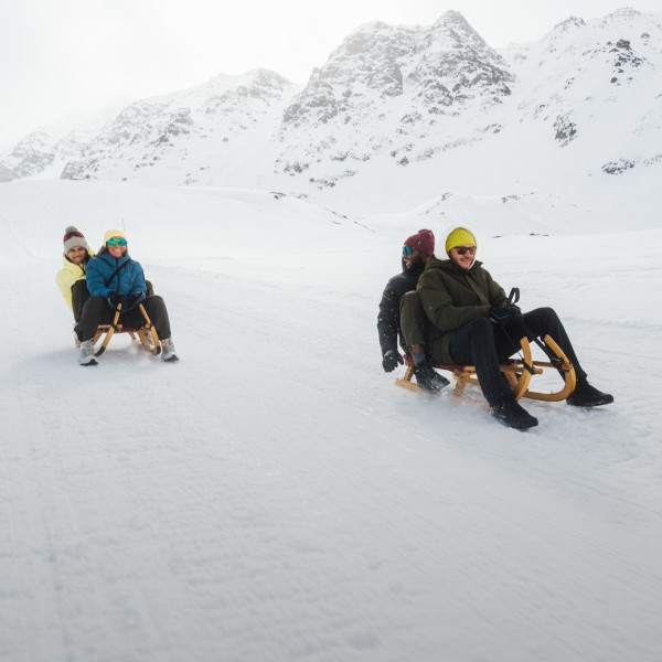 Drie personen zitten op een slee in de sneeuw.