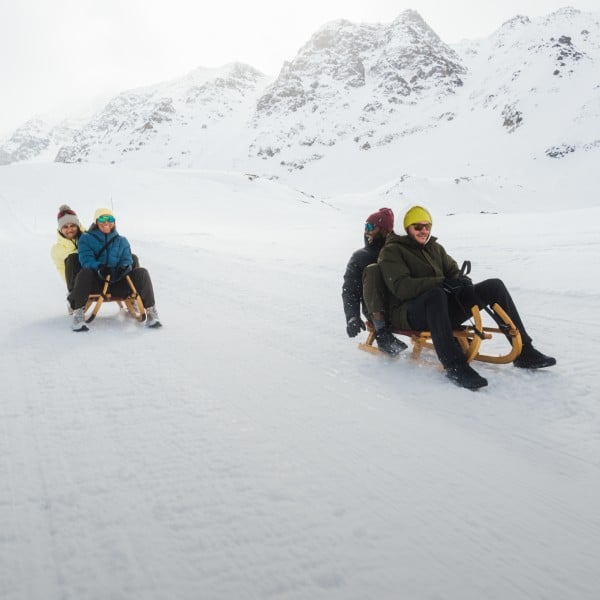Drie personen zitten op een slee in de sneeuw.