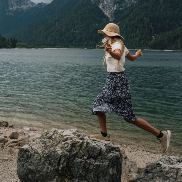 Une femme en tenue outdoor estivale en équilibre sur des pierres au bord d’un lac