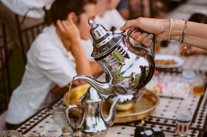 Een persoon schenkt thee in uit een zilveren theekan