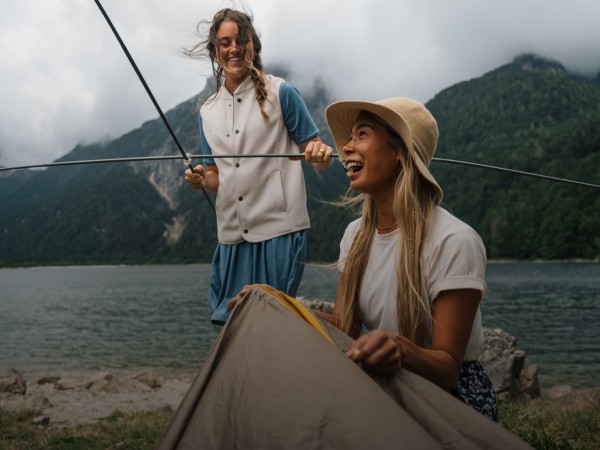Twee lachende vrouwen in een berglandschap zetten een tent op