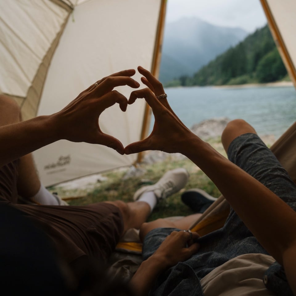 Twee personen liggen in een tent en vormen met hun handen samen een hart
